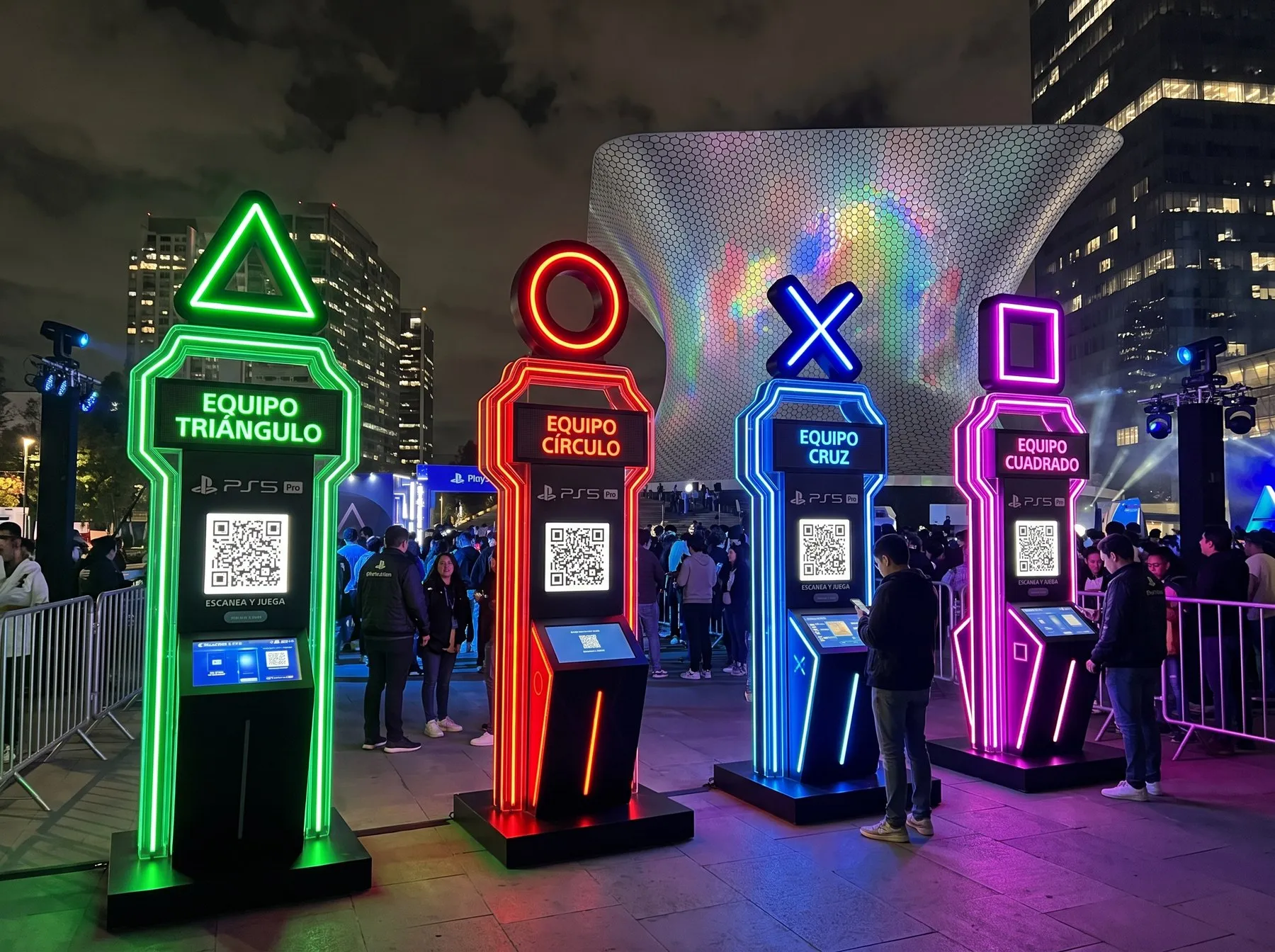 Cuatro tótems de registro con neón frente al Soumaya, uno por equipo (triángulo, círculo, cruz y cuadrado), con código QR y pantalla